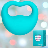 Displayed against a soft pastel background is the OhMiBod Lovelife Rev Finger Vibe, a teal heart-shaped item made from body-safe silicone with a loop. It is placed next to an OhMiBod Lovelife box, which has a heart-shaped window revealing a colorful pattern.